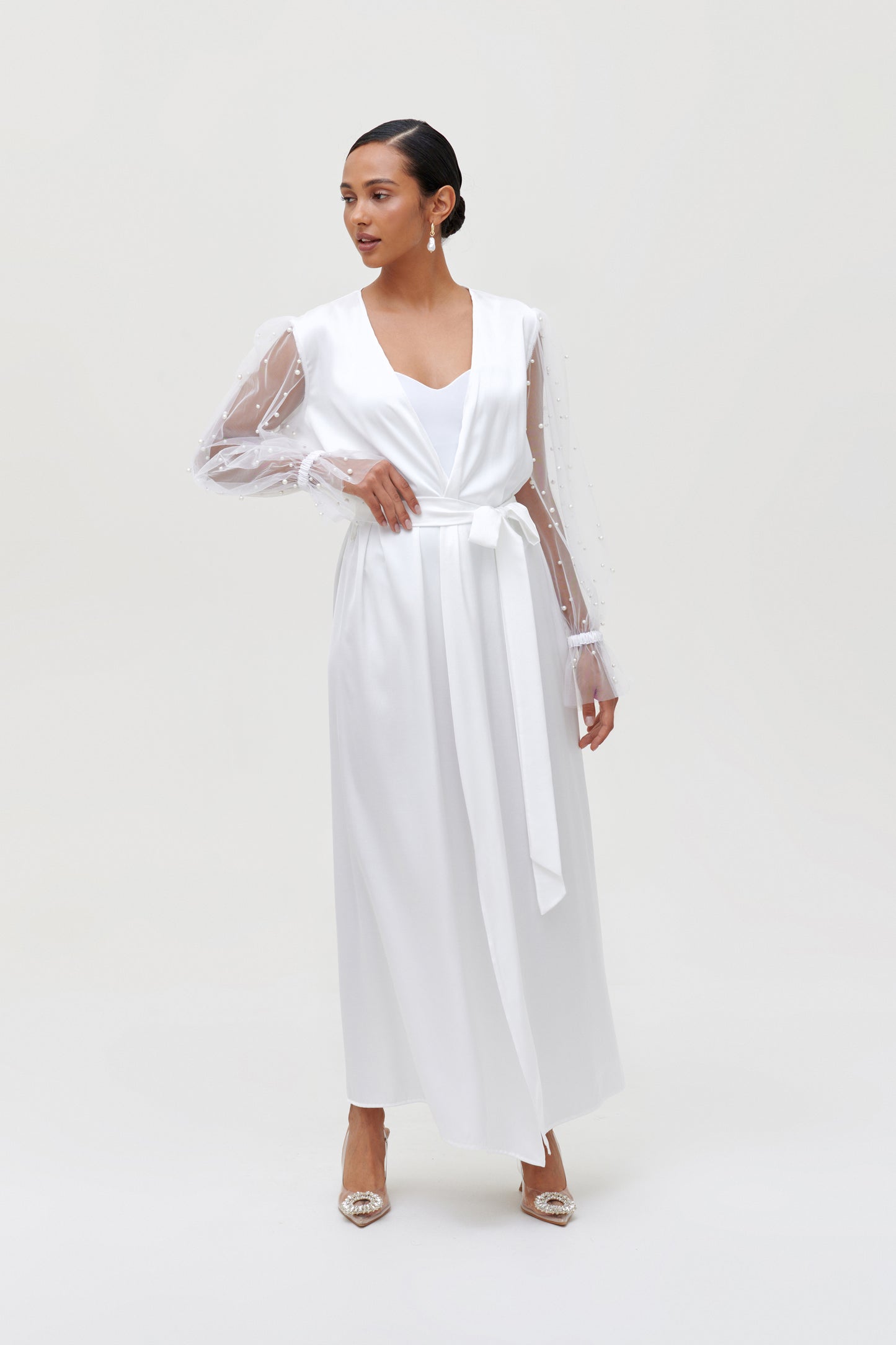 Elegant model in a white pearl bridal robe with satin fabric and pearl-adorned sleeves standing gracefully.