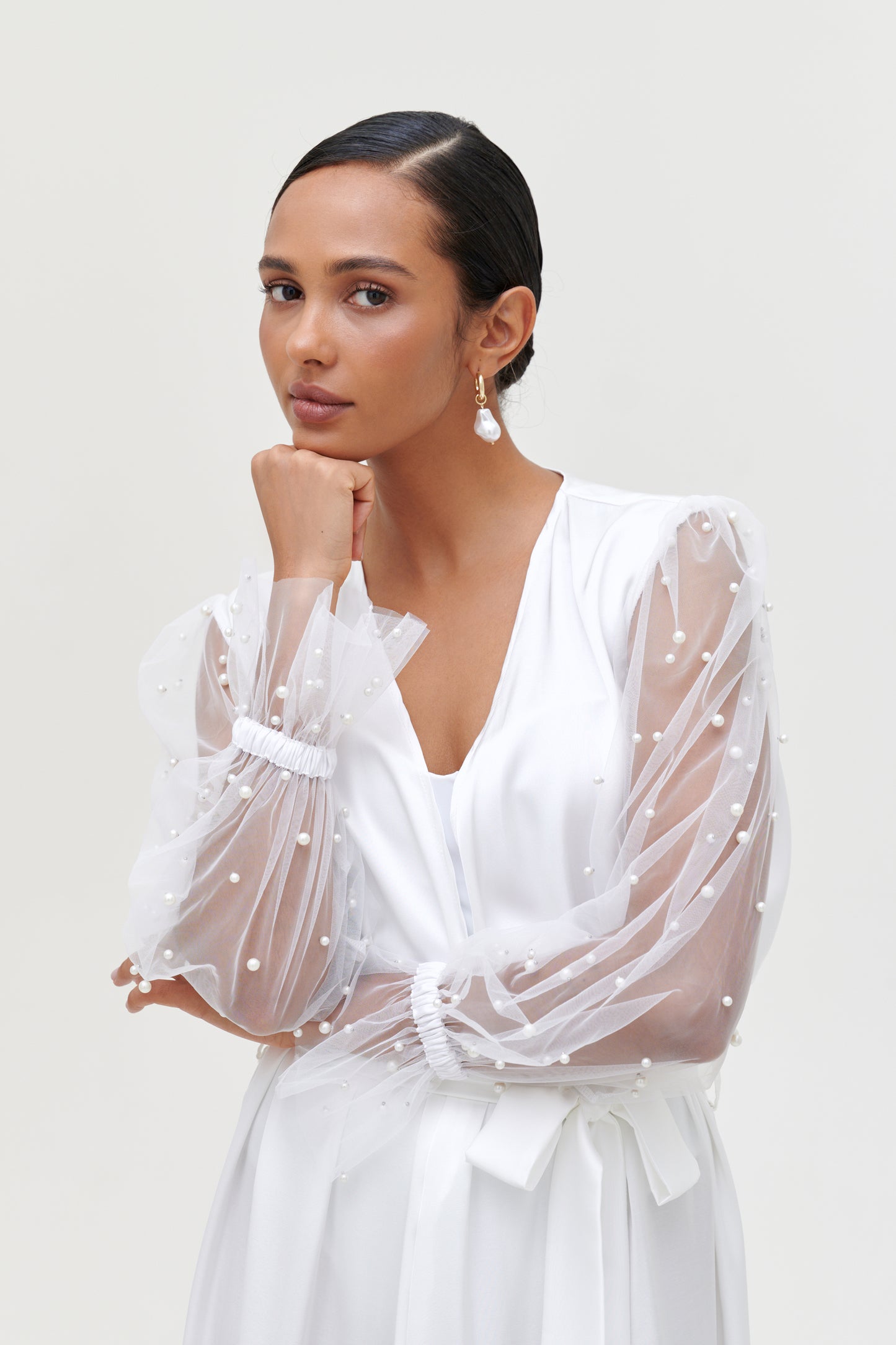 Model wearing a white pearl bridal robe with elegant pearl-adorned sleeves, showcasing refined elegance.